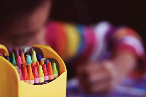 A box of crayons sits open with a child using them in the background