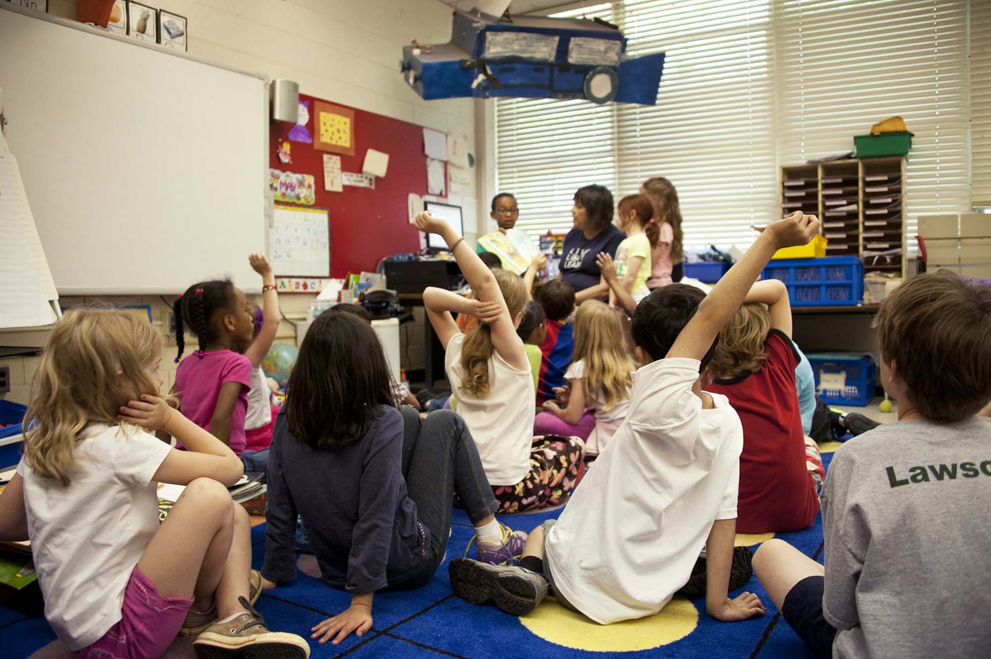 A number of children sit in a classroom and engage with their teachers.